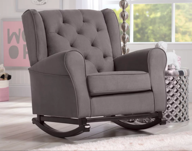 A gray plush rocking chair with rounded armrests and a tufted backrest, paired with metal curved legs resting on a hardwood floor