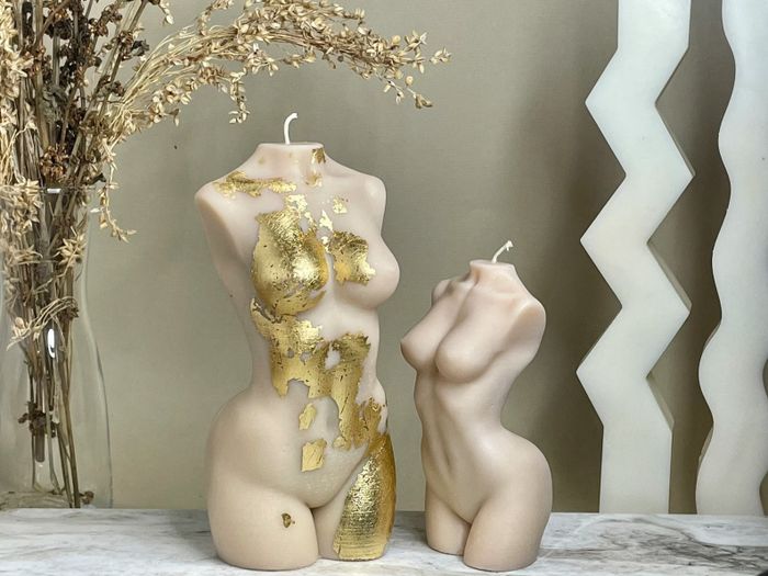Two nude Venus candles, one shorter than the other, with the taller one featuring delicate gold flakes