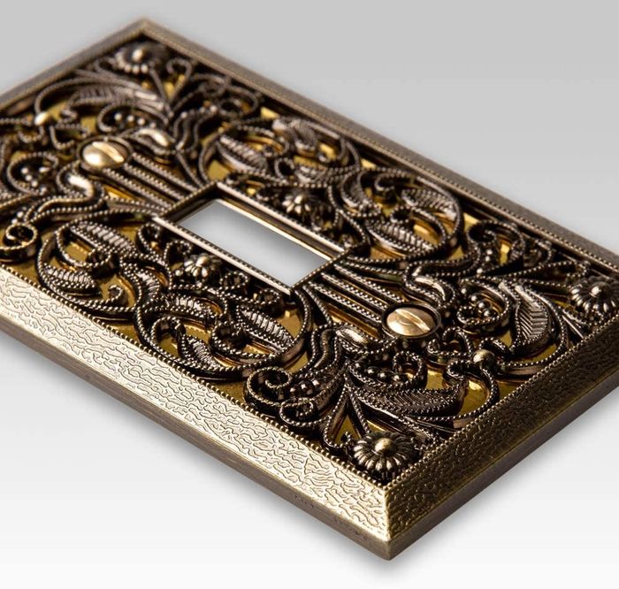 A close-up view of a brass wallplate cover, showcasing the intricate filigree design
