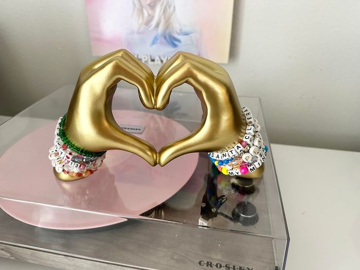 A reviewer image showing two hands forming a heart with beaded bracelets from Taylor Swift's Eras tour.