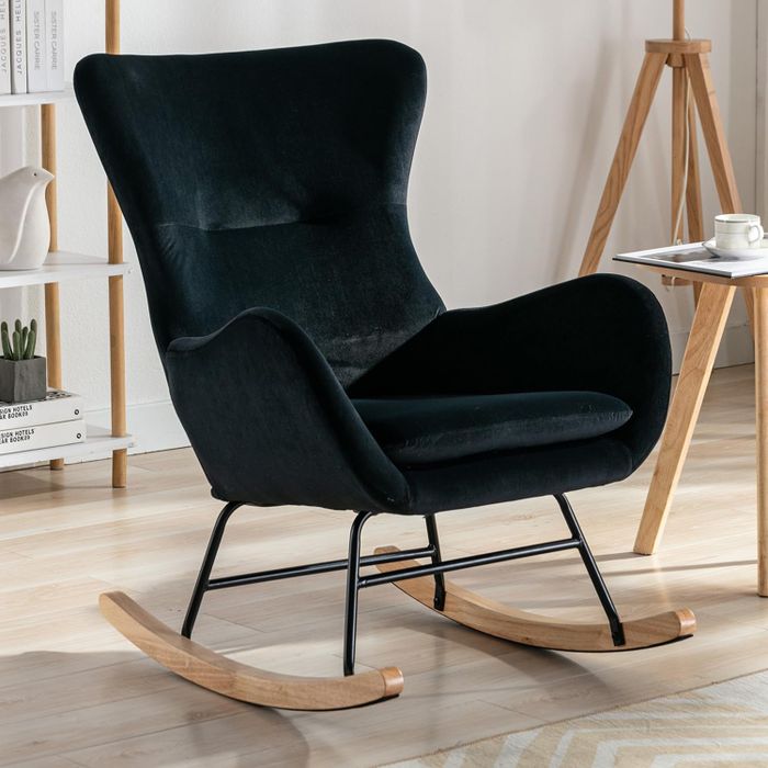 A black upholstered rocking chair with wooden rockers placed in a sleek, modern room. Nearby is a small table with a cup, an easel, and a bookshelf