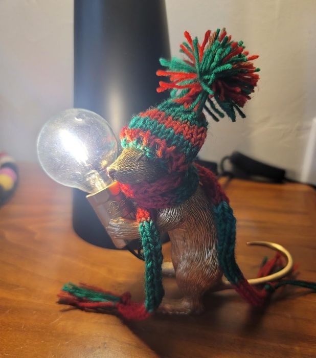 A charming mouse figurine, donned in a knit hat and scarf, holds a light bulb in its tiny paws.