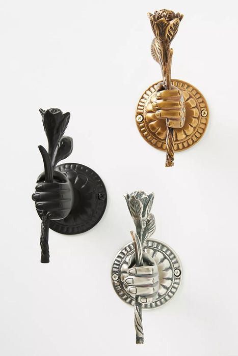 Three wall hooks in black, bronze, and silver, each shaped like a hand holding a flower