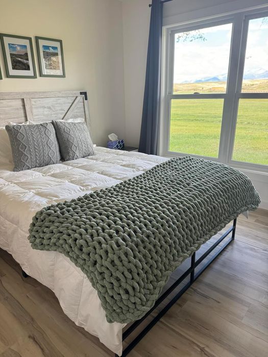 A reviewer’s beautifully made bed featuring a chunky knit blanket elegantly draped at the foot of the bed