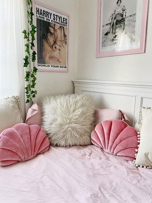 Pink seashell-shaped pillows atop a bed with gray fur pillows and pink sheets