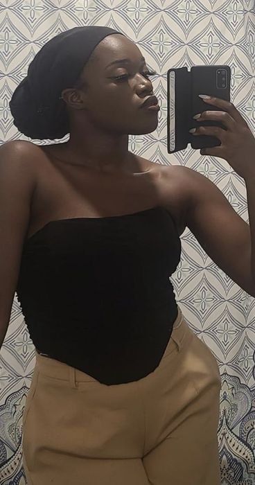 Person snapping a mirror selfie, dressed in a strapless top and high-waisted pants, holding a smartphone