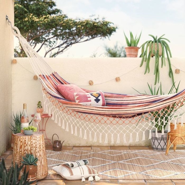 a fringe hammock in two colors hanging in a lush backyard