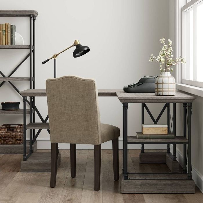 A gray wood writing desk placed next to a chair and a bookcase