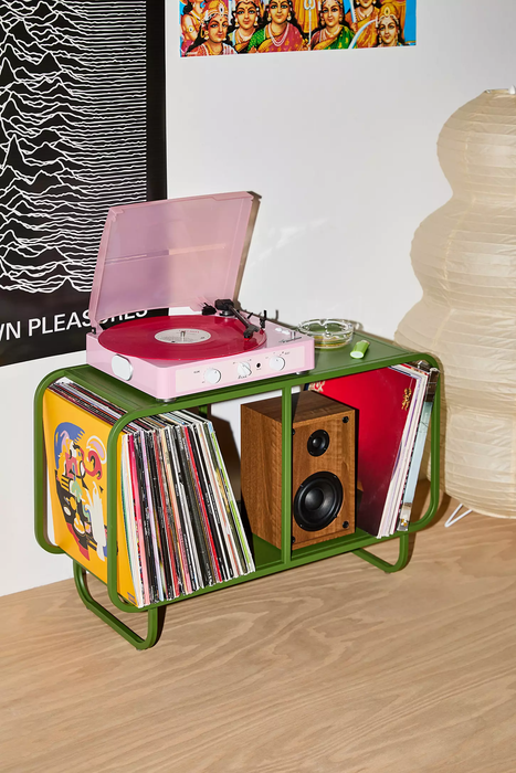 A vinyl record player placed on a stand alongside a speaker and a collection of records. Stylish and modern room design