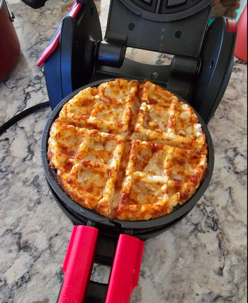 Waffle pizza cooking in a waffle maker on a marble kitchen counter
