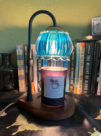A charming lamp with a stained-glass shade rests on a table next to a lit candle, with a row of neatly stacked books on a nearby shelf.