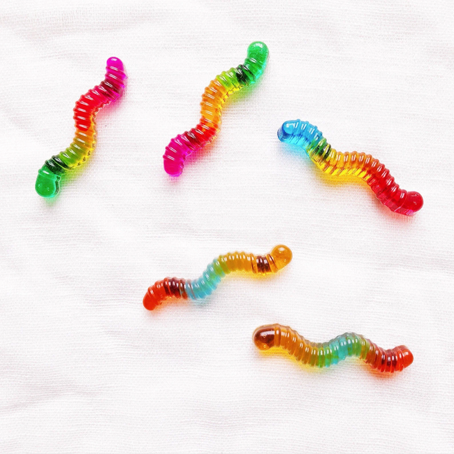 Five vibrant gummy worms resting on a white surface.