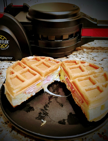 A waffle sandwich with ham and cheese on a plate, sitting next to a waffle maker
