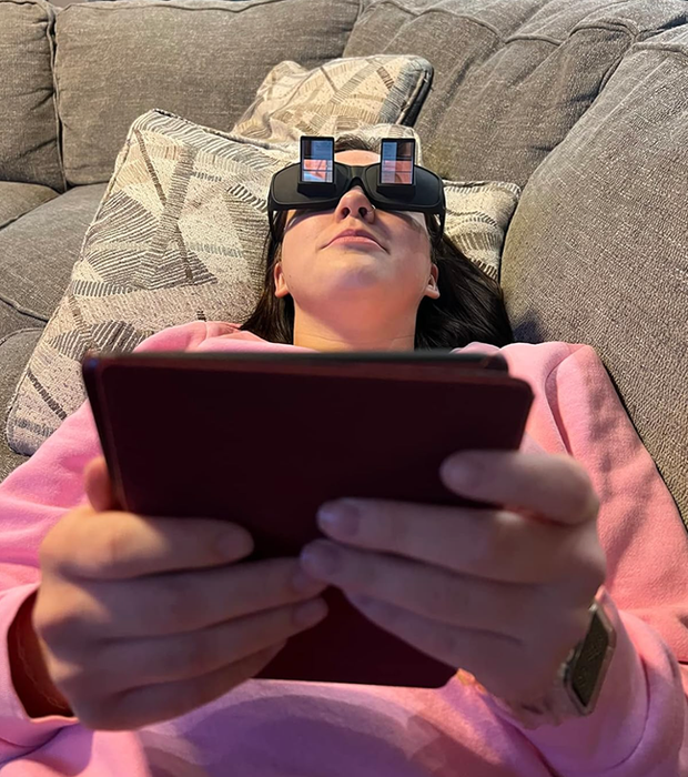 A reviewer lounging on the couch, reading a book while using the horizontal glasses to keep the book upright