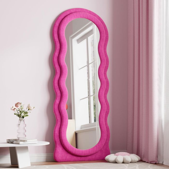 A full-length mirror with a soft, plush pink border, beautifully set in a minimalist room with a vase of flowers on a side table.