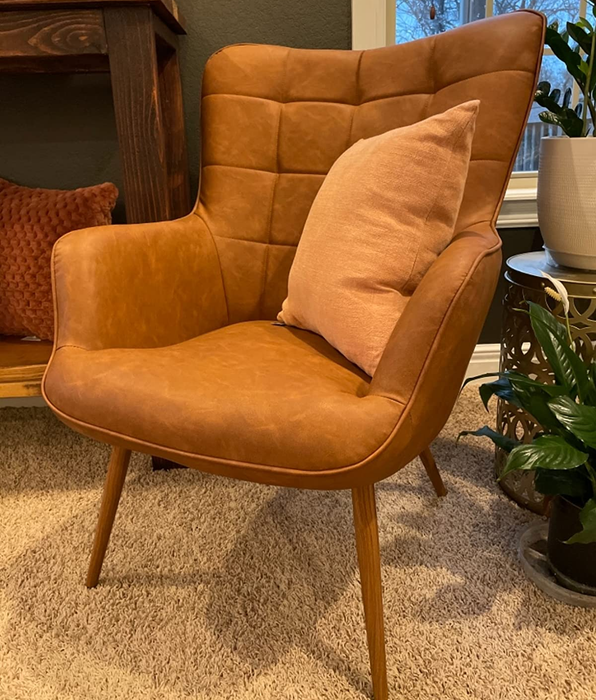 A close-up reviewer photo of a faux leather chair with a pillow resting on it.