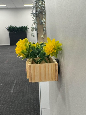 A wooden wall-mounted planter adorned with yellow flowers, placed in an office hallway.