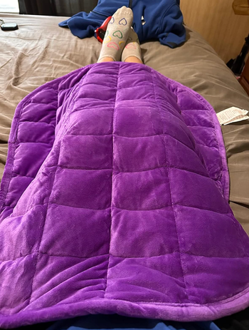 A purple weighted blanket rests comfortably on a reviewer's legs.