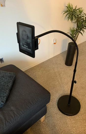 Adjustable floor-standing tablet holder placed next to a couch, showing 