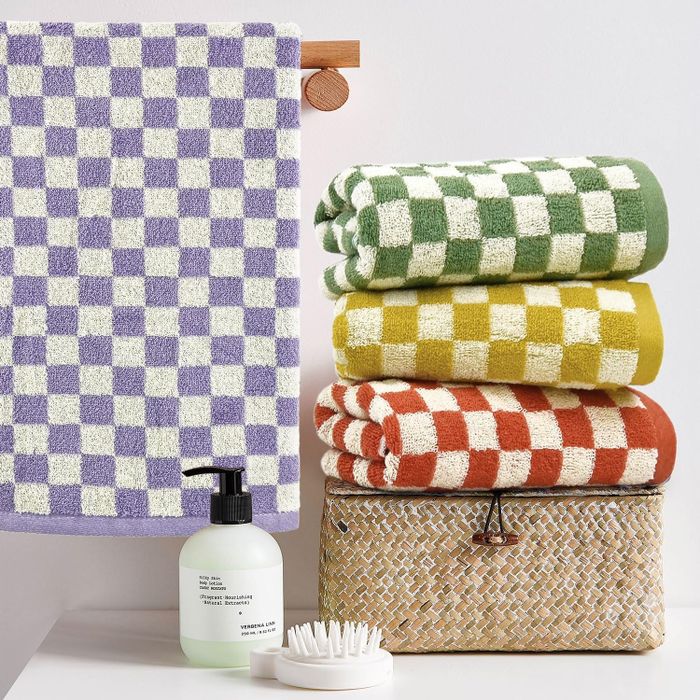 A stack of checkered towels in purple, green, yellow, and red placed on a woven basket next to toiletries.