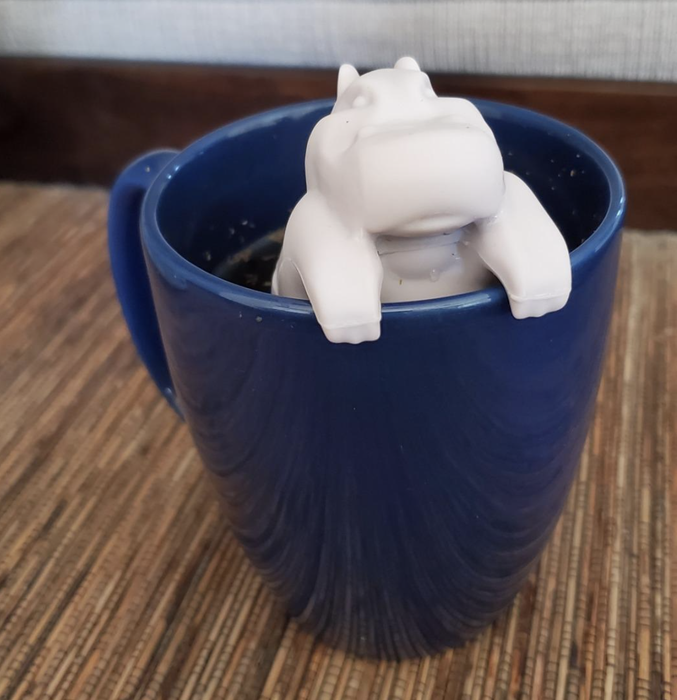A gray hippo-shaped tea infuser resting on the edge of a mug