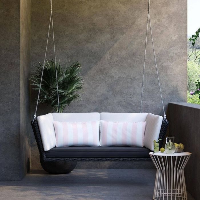 A loveseat swing with black and white cushions beside a small table