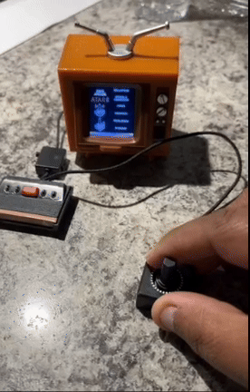 A person playing a retro Atari video game on a mini TV replica, using a joystick and console
