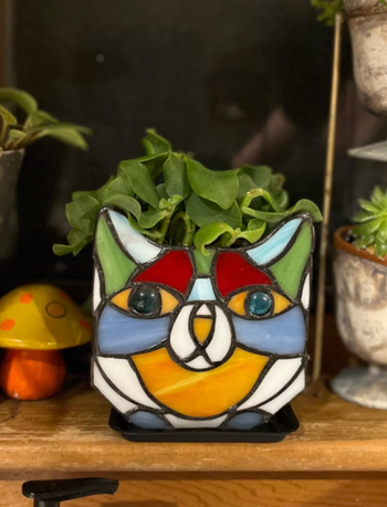 A stained glass cat-shaped planter, holding a green plant, surrounded by charming decor pieces like a mushroom ornament.