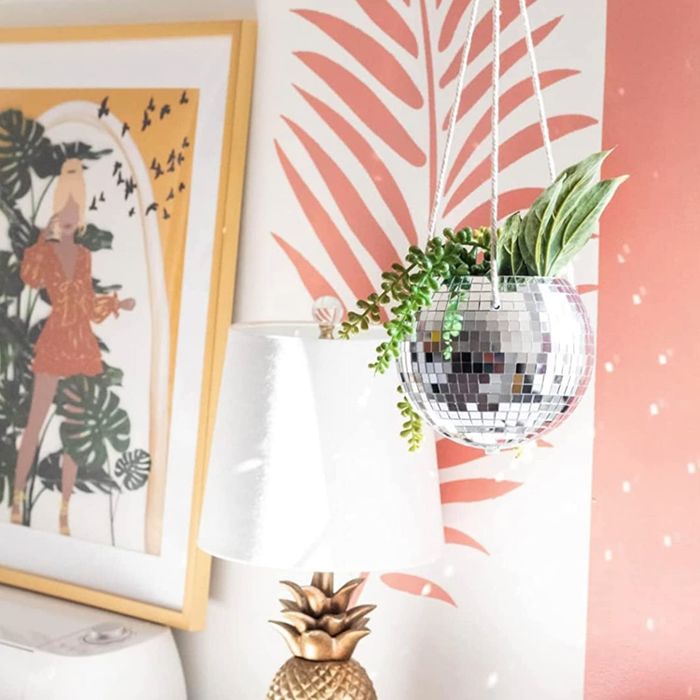 The disco ball planter suspended in front of vibrant, tropical pink wallpaper, bringing an extra sparkle to the room.