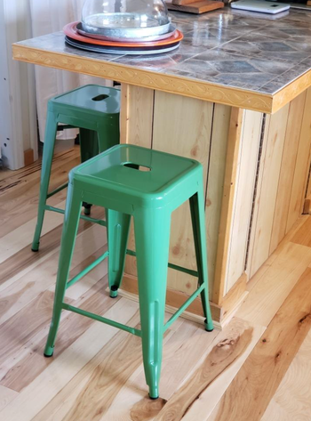 Two green metal bar stools placed at a wooden kitchen island with a tiled countertop.