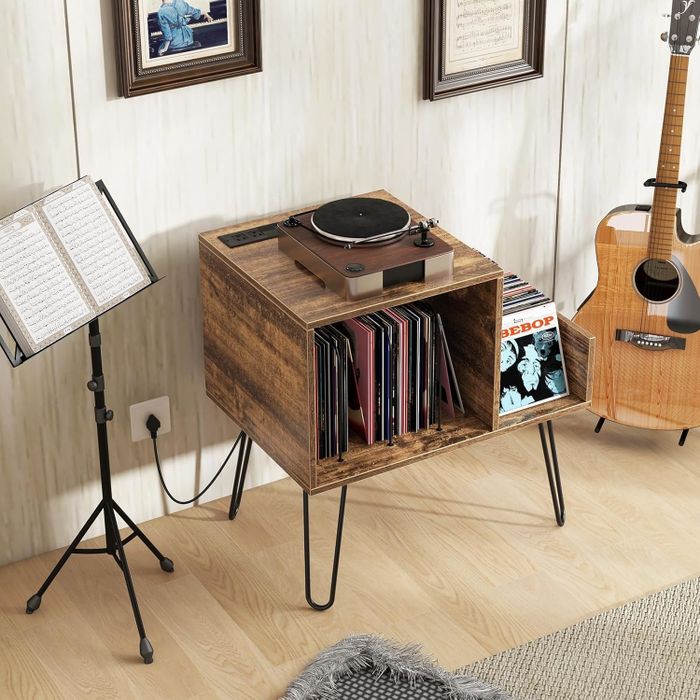 Turntable placed on a wooden stand alongside vinyl records, next to a guitar and music stand, creating a cozy and musical ambiance in a shopping setting