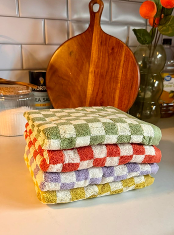 A pile of checkered kitchen towels on a counter with cooking utensils in the background.