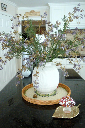 A white spherical vase holding delicate flowers on a kitchen counter, placed on a circular woven tray next to a decorative mushroom ornament.