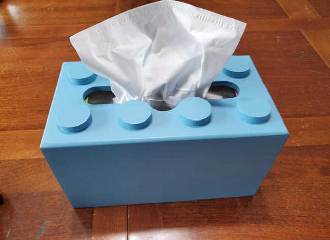 A tissue box shaped like a building block resting on a wooden table.