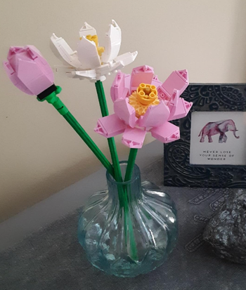 Three LEGO flowers elegantly arranged in a clear vase, accompanied by a framed image of an elephant and an inspiring quote.