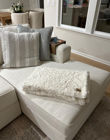 A soft, textured throw blanket gently draped over a sleek, modern sectional sofa in a minimalist living room space, exuding elegance and comfort.
