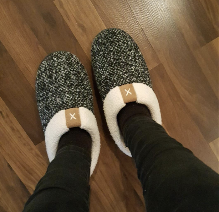 A reviewer wearing slip-on white and black marled slippers with a cozy fleece lining