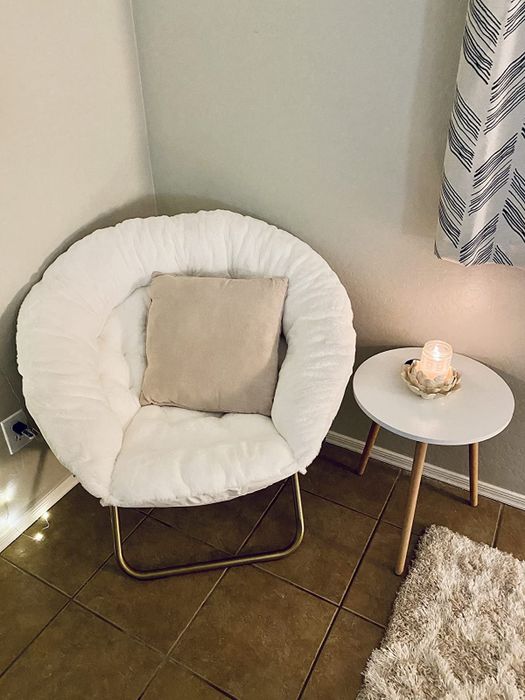 A reviewer's photo of a white saucer chair positioned next to a side table with a lit candle on it.