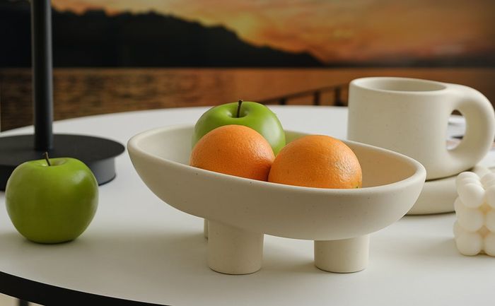 A small ceramic fruit bowl with three sturdy legs, adding a touch of charm to any countertop.