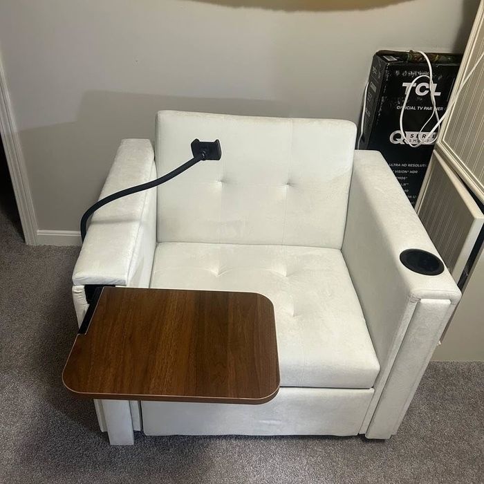 White armchair featuring an attached wooden swivel table and black charging cable.