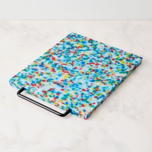 A speckled cutting board with a convenient handle resting on a marble countertop.