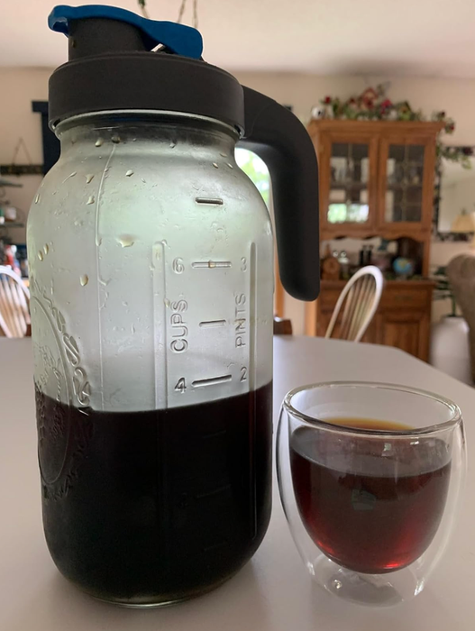 A clear-handled pitcher of cold brew coffee placed beside a cup filled with freshly brewed cold coffee.