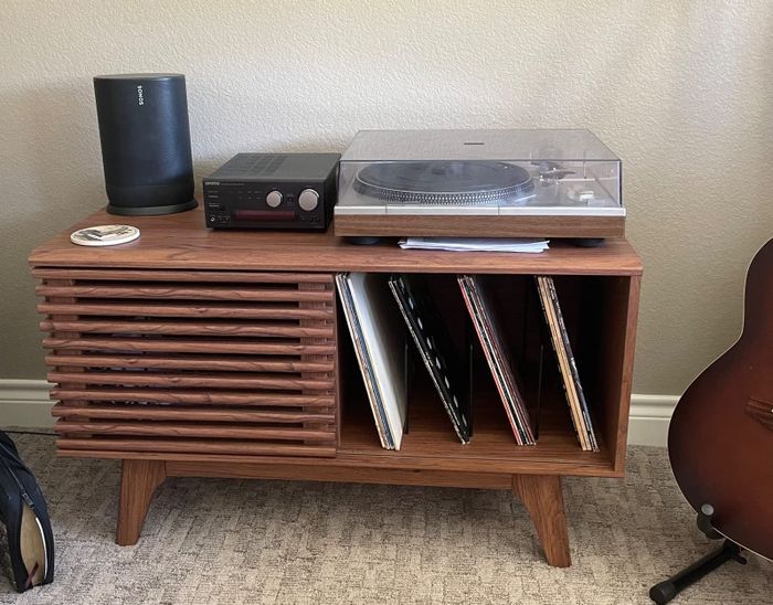 Reviewer image of a wide brown wooden record player stand with a sliding door and the record player placed on top