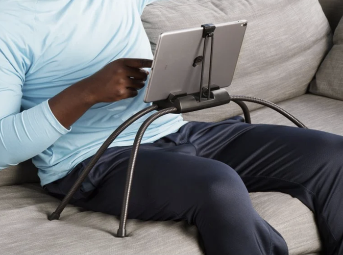 A model using the flexible black four-legged stand on a couch, with their tablet hovering comfortably above their lap