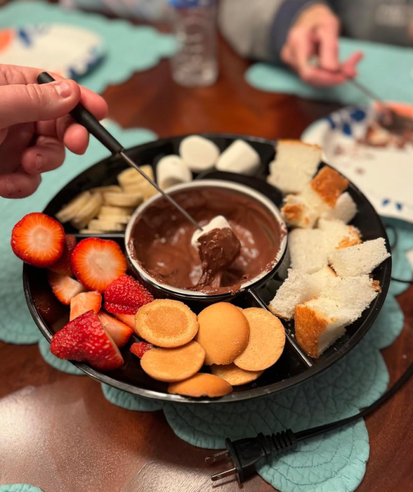 A platter of assorted snacks (strawberries, cookies, marshmallows, and cake pieces) surrounding a bowl of decadent chocolate fondue