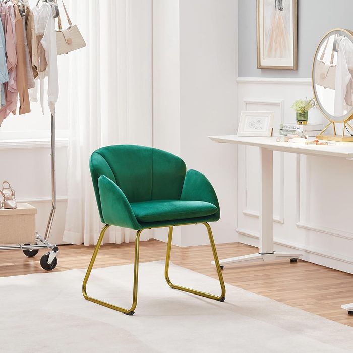 A green upholstered chair with gold legs, beautifully arranged in a chic, modern dressing room setting.