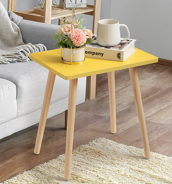 A cozy living room with a small wooden table featuring a mug, a book, and a vase of fresh flowers.