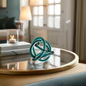 A glass sculpture with intertwined loops placed on a round table, next to a stack of books and a lit candle, creating a cozy ambiance in the room.