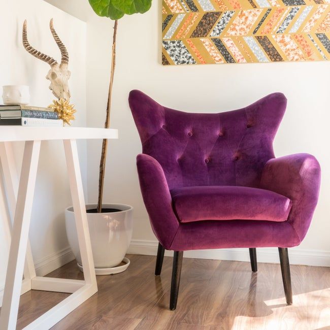A photo of the purple velvet butterfly armchair in the corner of a room.