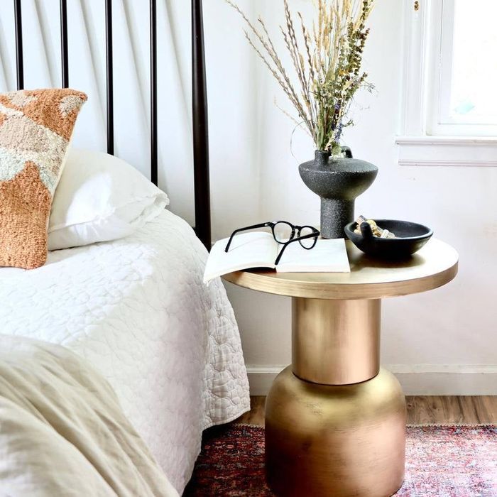The antique brass finish accent table placed beside a bed
